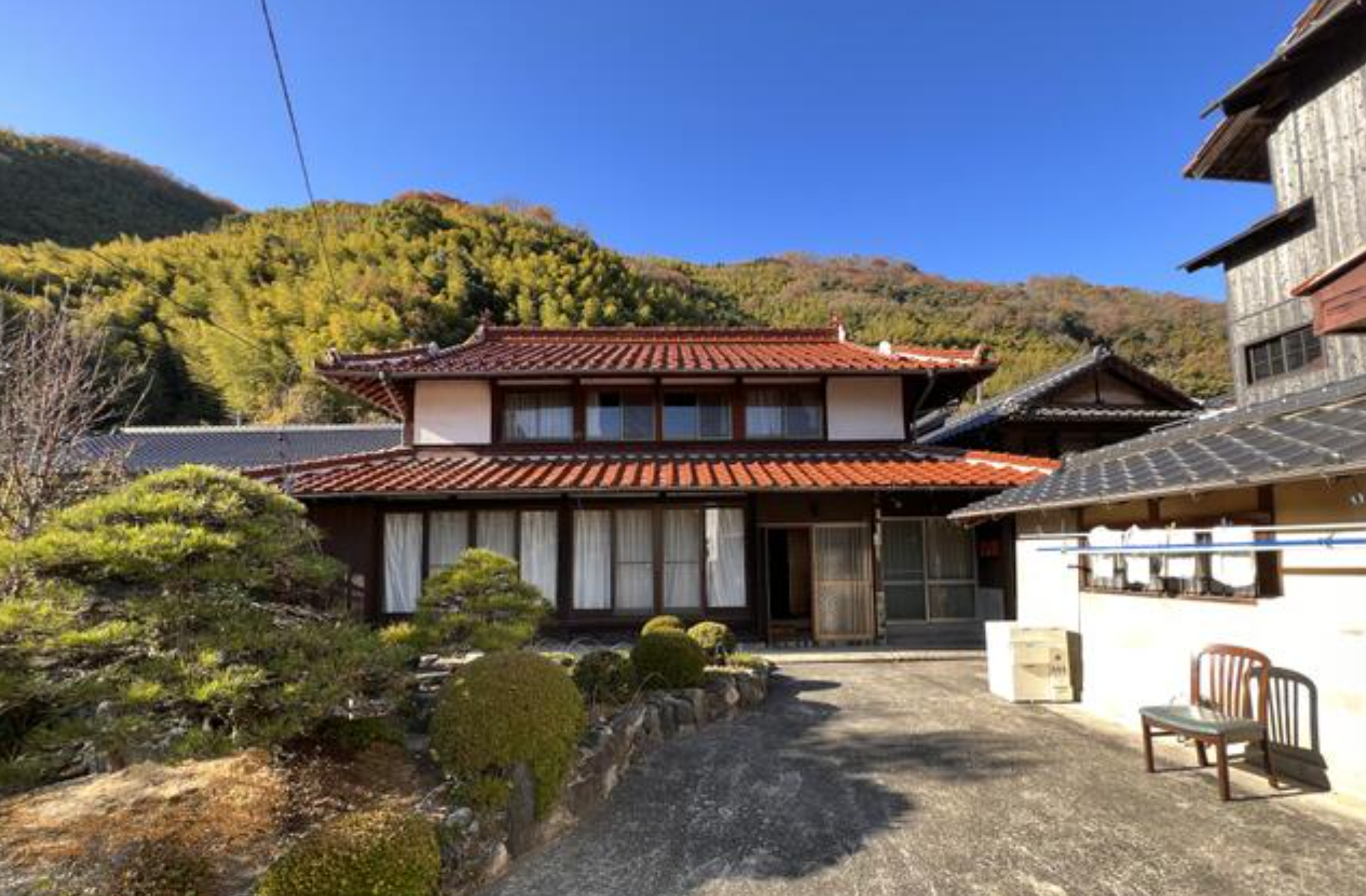A traditional Japanese farmhouse (akiya) with a tiled roof, set against forested hills